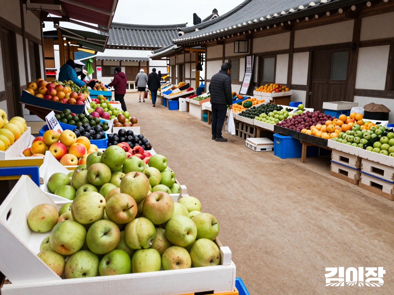 밝은 낮의 한국 전통시장 통로 앞에 배와 사과 상자가 놓이고 뒤로 여러 농산물 판매대가 이어진 모습