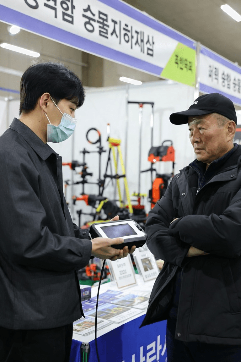 농기구가 놓인 부스에서 두 사람이 태블릿을 보며 대화하는 모습