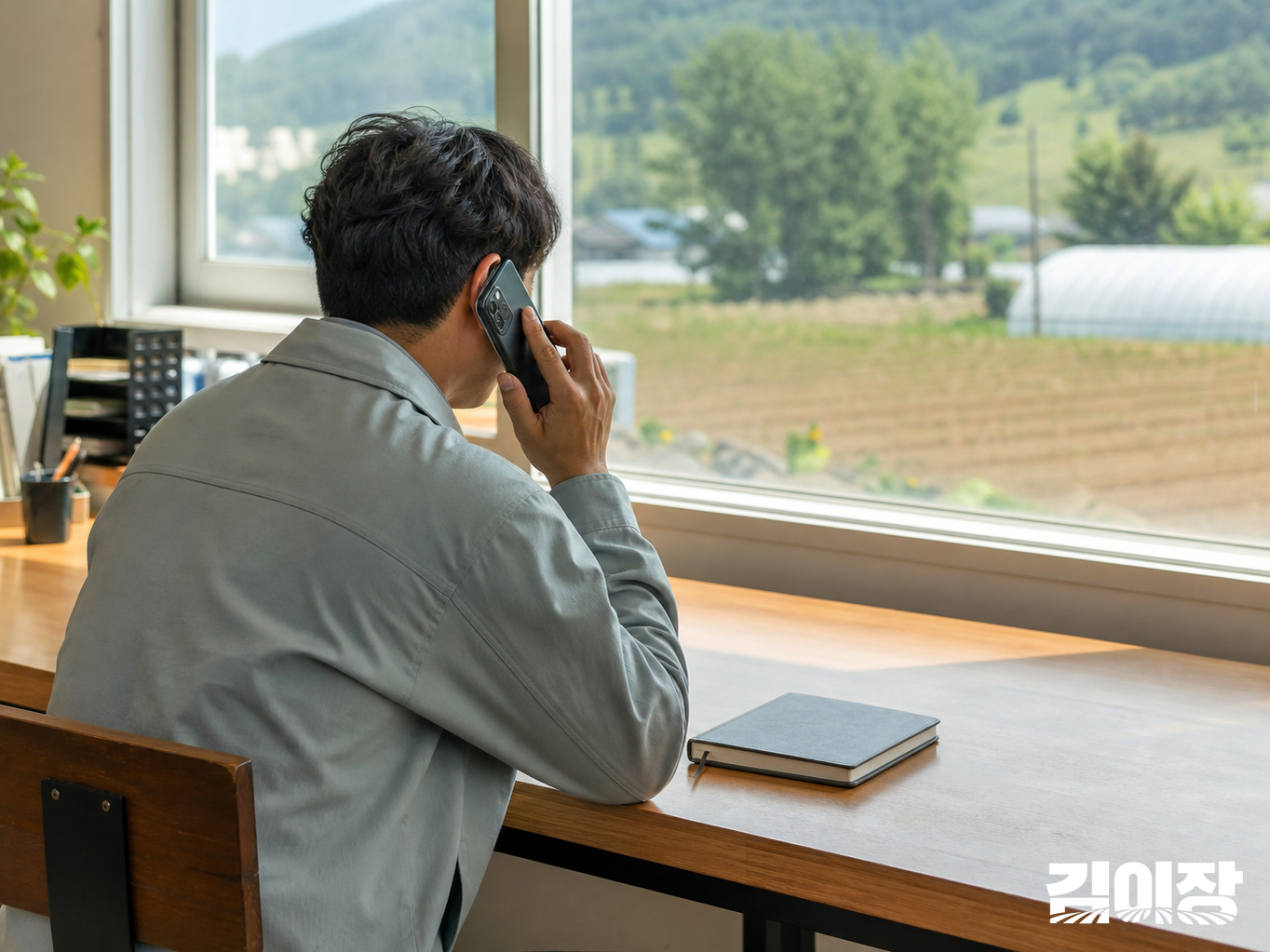 농가 사무 공간에서 닫힌 기록장 옆에 앉아 전화하는 사람을 옆뒤에서 바라본 모습