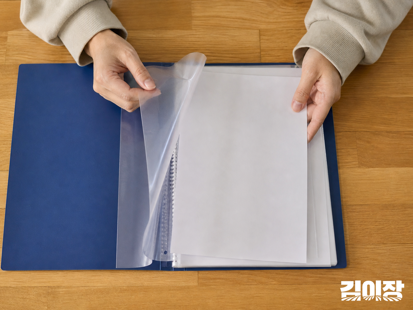 책상 위 짙은 청색 보관철의 투명 속지에 뒷면이 보이는 종이를 정리하는 손