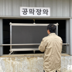 산란계 시설 외곽에서 주민 한 명이 축사 외벽의 큰 공기정화 설비를 살펴보는 개념 장면
