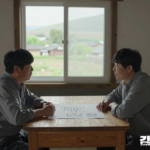 마을회관 창가 탁자에서 주민 두 명이 주거 공간이 표시된 단순한 마을 배치도를 함께 살펴보는 설명용 장면